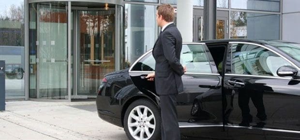 A professional chauffeur opening the door of a luxury black sedan for a premium chauffeur service in St. Louis