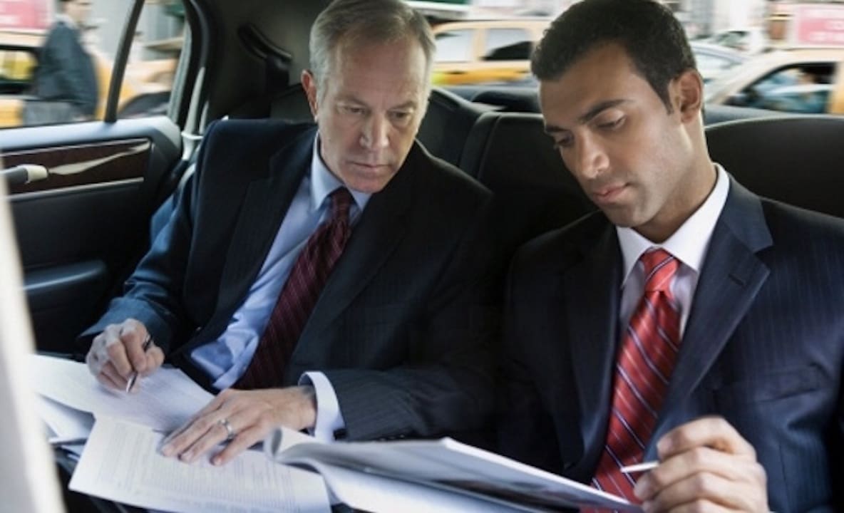 Hourly Service Business executives reviewing paperwork in the backseat of a luxury sedan during an airport limousine service trip in St. Louis.